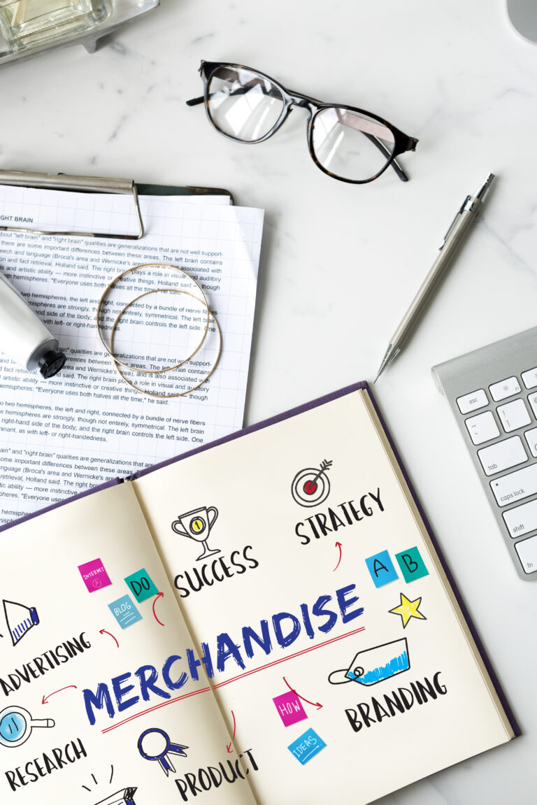 Flat lay of a modern workspace with glasses, documents, a pen, a keyboard, and an open notebook showing hand-drawn strategy and branding illustrations.